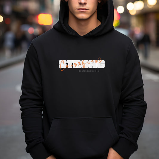 Black heavy weight hoodie with the graphic  Strong courageous. Strong is in large white text overlayed with orange script text for courageous. Underneath is the scripture reference. Deuteronomy 31:6